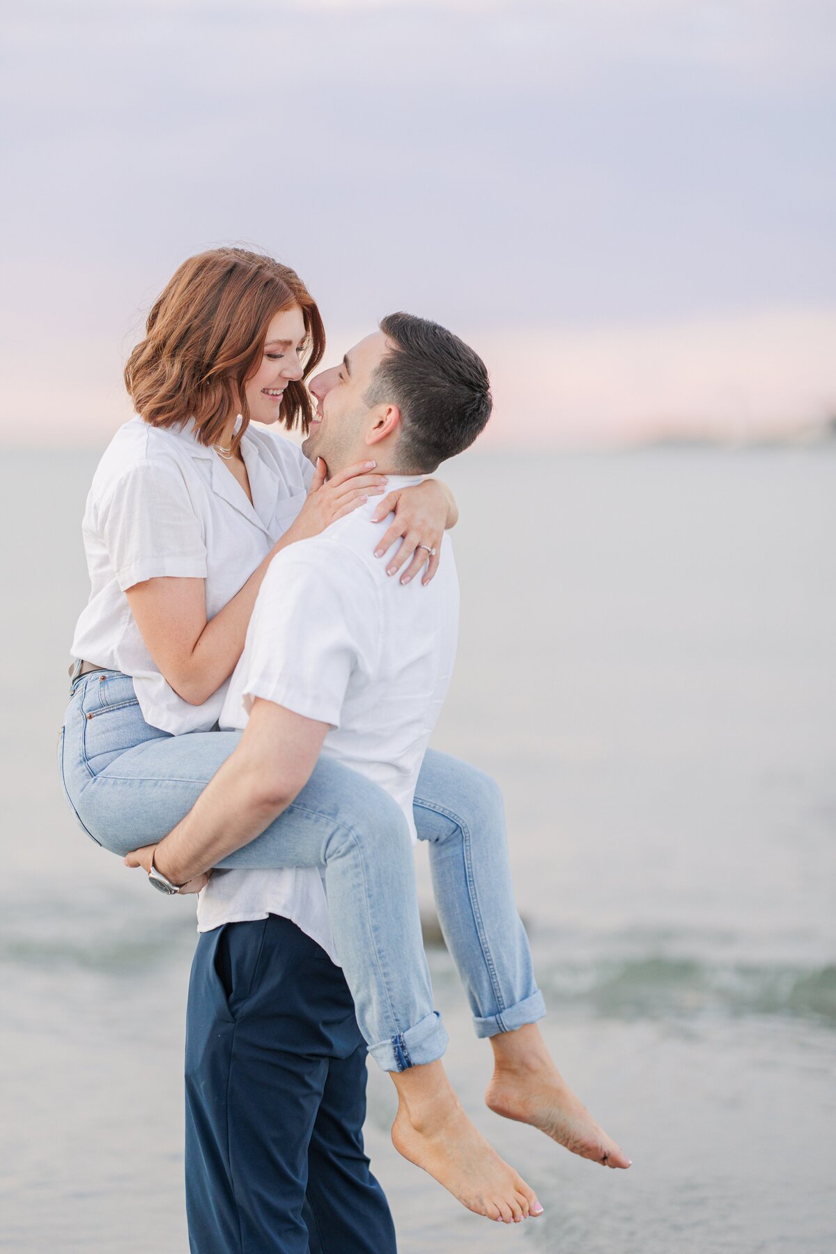 A man picking up and laughing with a woman during Wingaersheek Beach sunset photos.