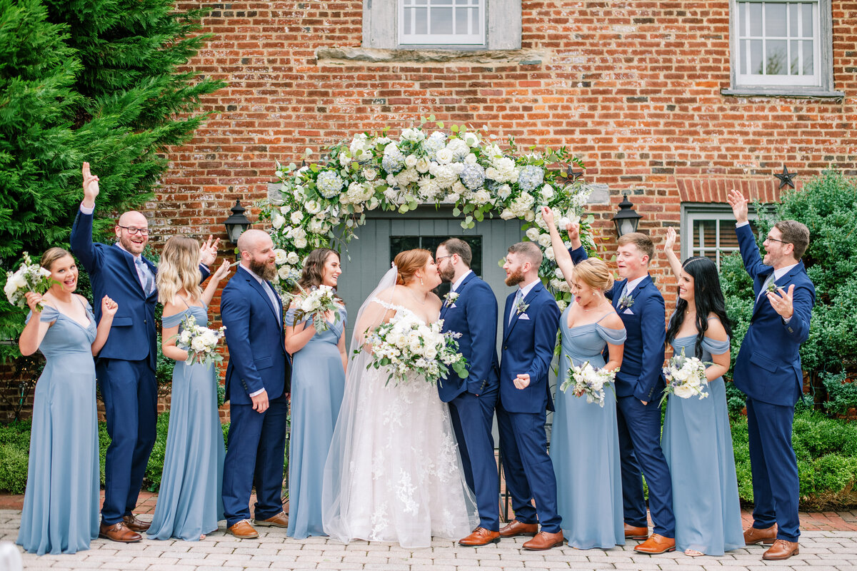 Blue and white wedding arch behind wedding party holding bouquets