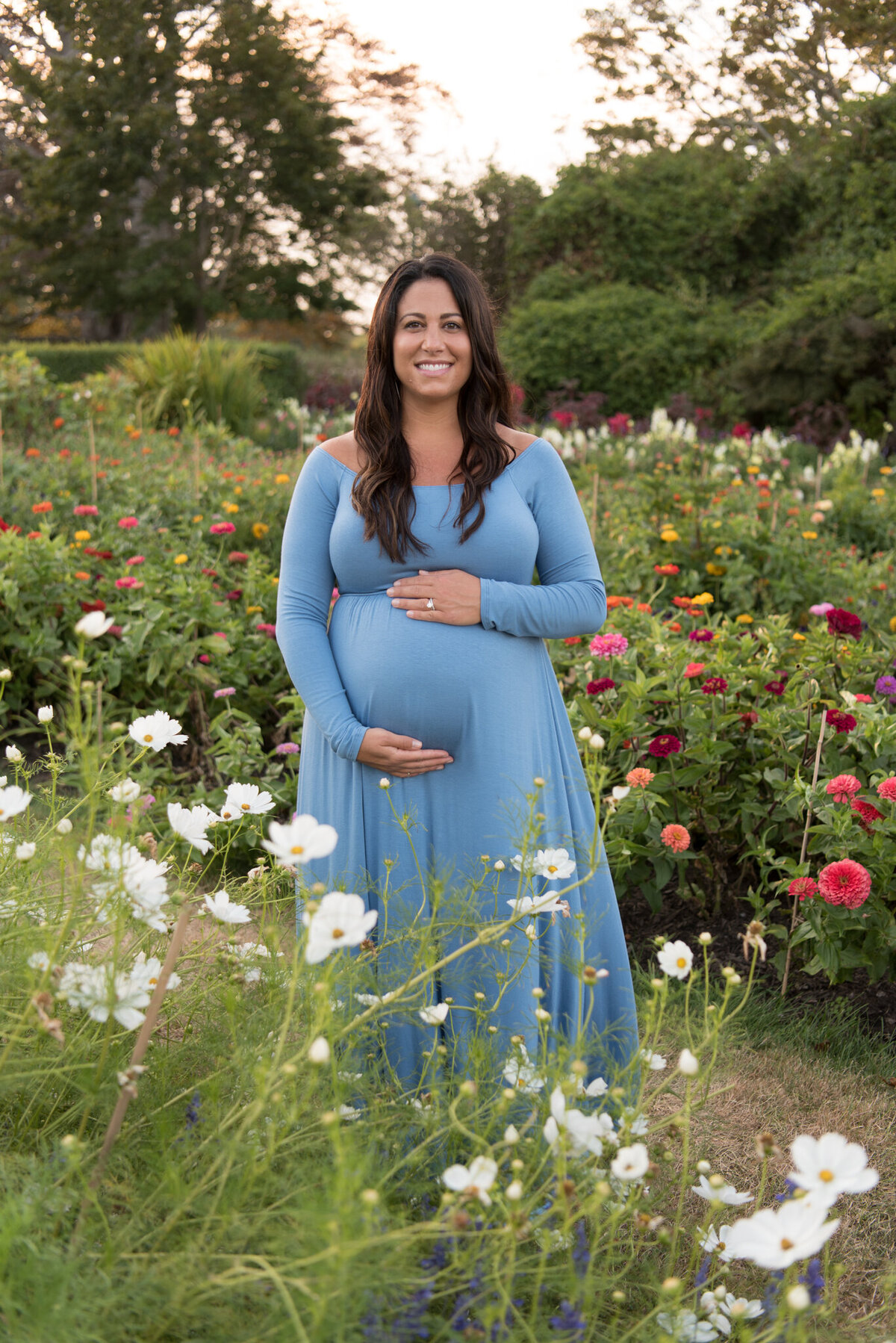 A pregnant mother is smiling at the camera in a garden of wildflowers in bloom