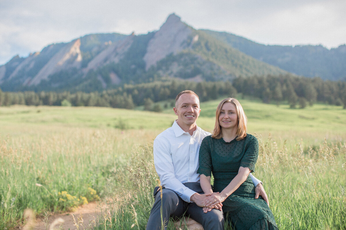 An engaged couple smile for a portrait in a green field at Chautauqua Park