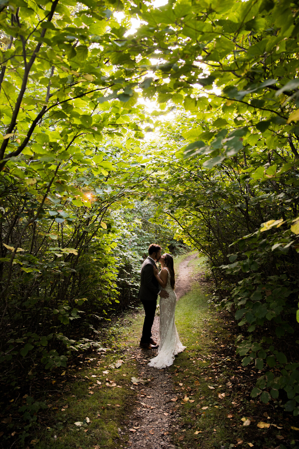married couple kisses while they walk through a tunnel of leaves 