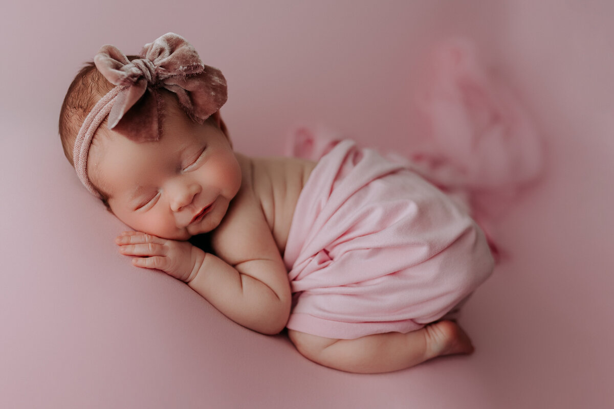 newborn girl wearing bow with pink backdrop