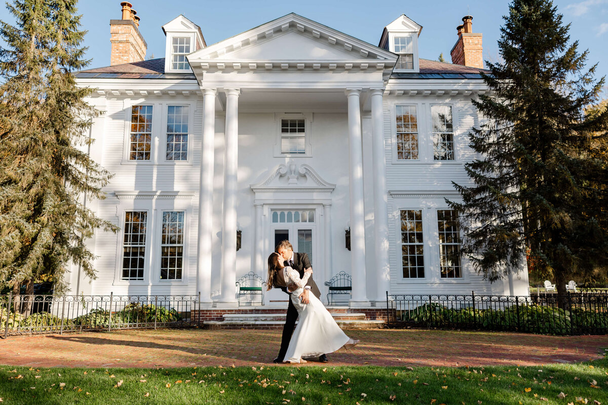 A bride and groom share a romantic dip outside a historic mansion in Stowe, Vermont, capturing a timeless moment during their elegant wedding celebration