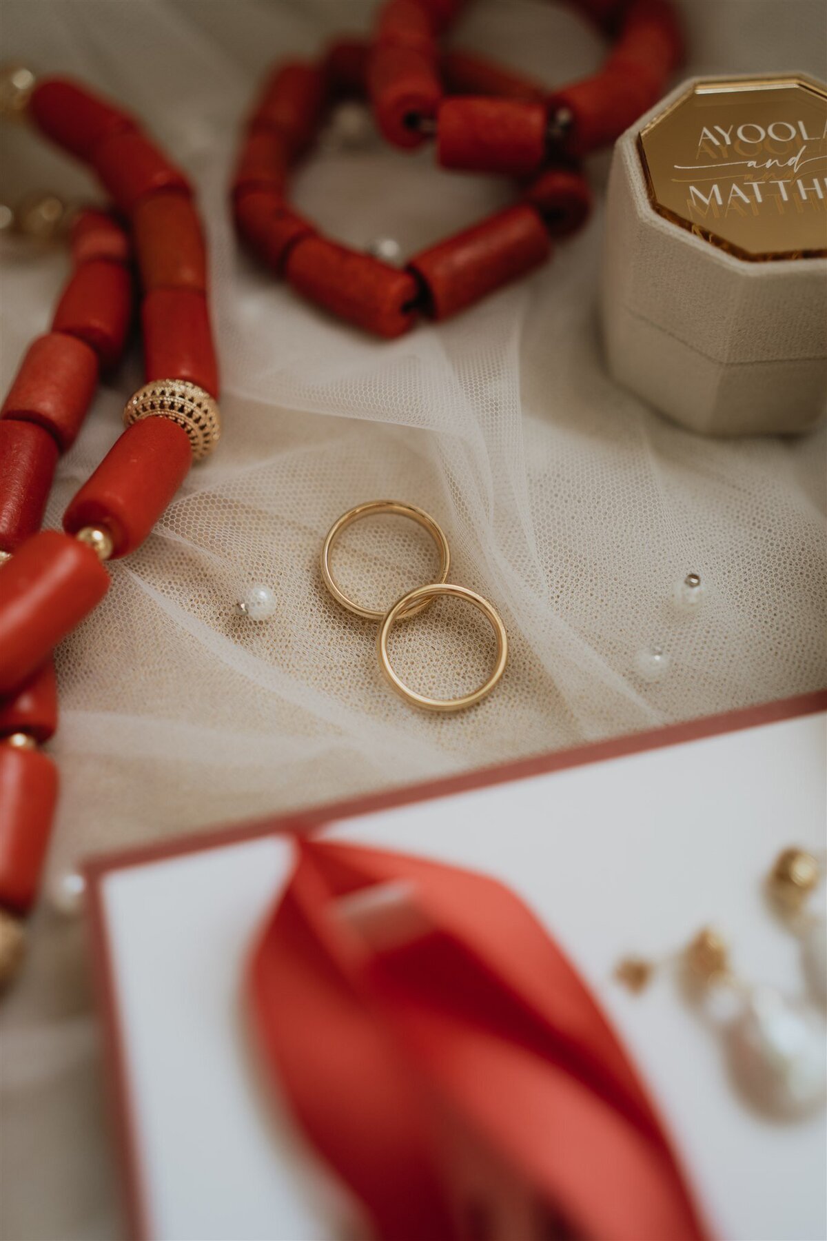 Wedding rings are photographed on top of a veil. They are surrounded by jewellery an wedding stationary.