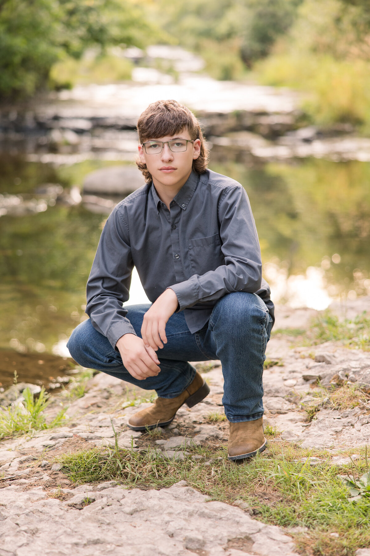 Senior guy squatting next to a river looking at the camera