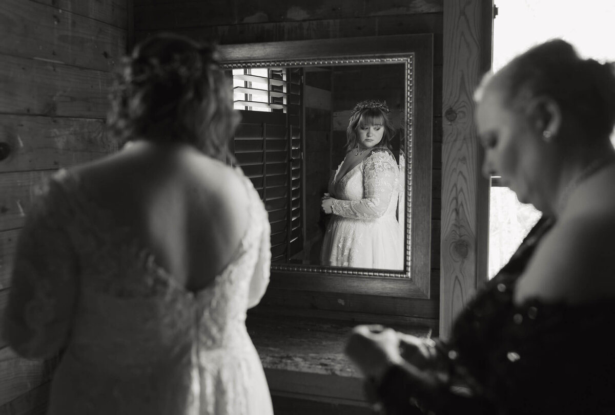 documentary wedding photograph of the bride in the reflection of a mirror watching her mother fixing her wedding dress 