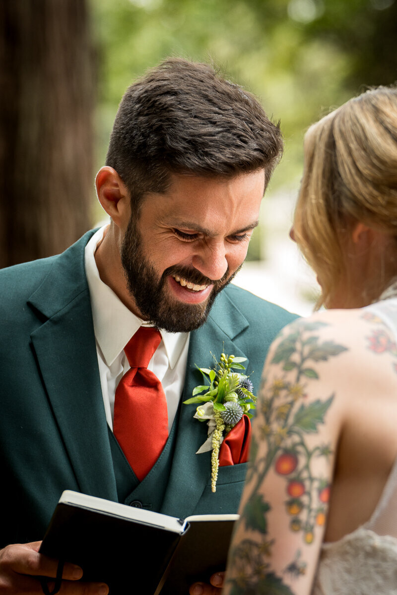 A joyful moment as the groom bursts into laughter while delivering his heartfelt vows in the serene redwood grove at Ridgefield in Arcata. This candid wedding photo perfectly captures the love and lightheartedness of their special day, surrounded by towering redwoods and cherished family and friends.