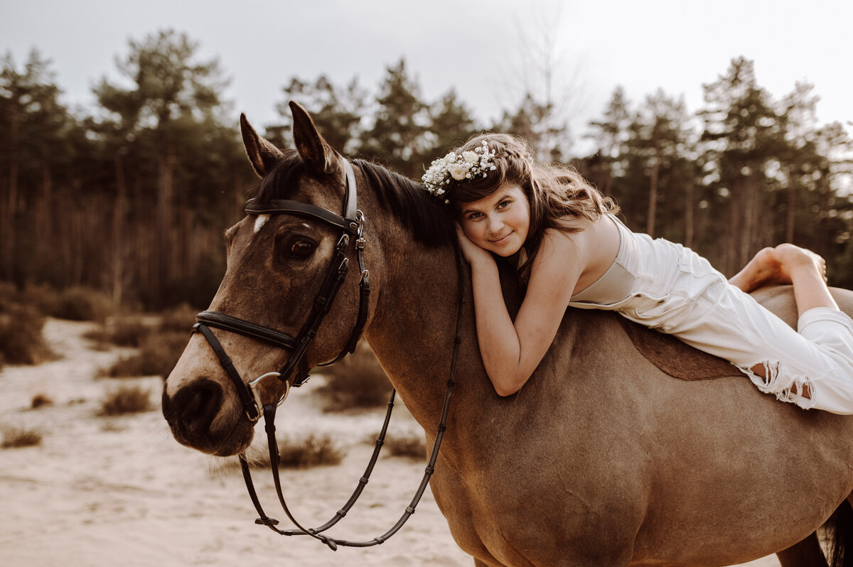 Meisje ligt op paard en heeft bloemenkroon
