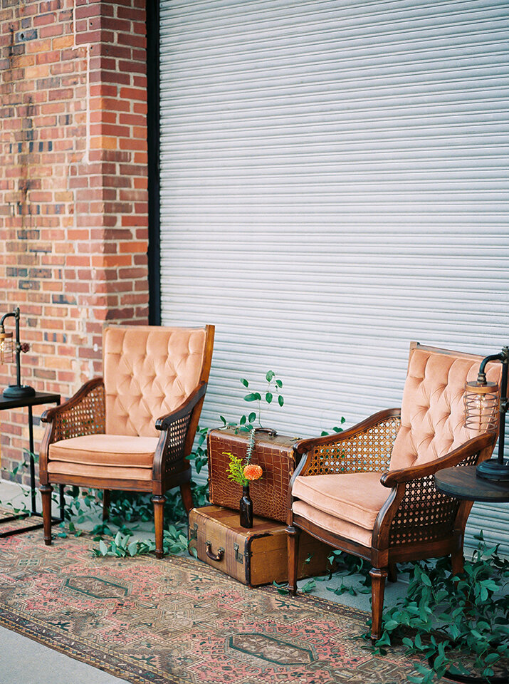 Two blush-colored chairs with suitcases and garland atop a carpet outside.