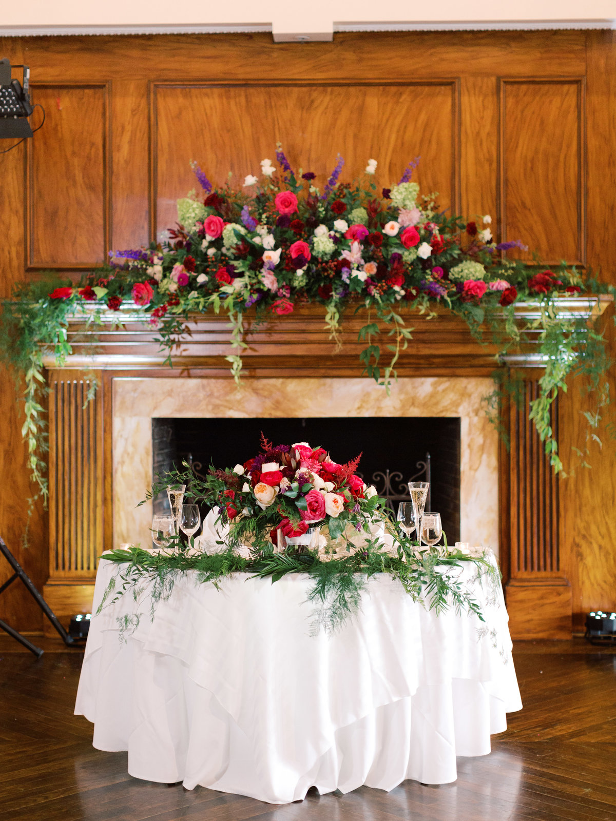 Sweetheart table with jewel toned flowers and a mantel floral arrangement as a backdrop