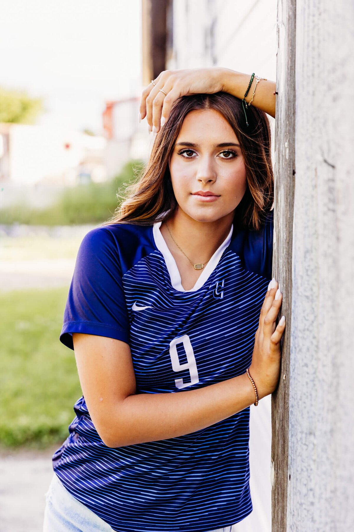 gorgeous teen girl leaning against a wall and looking super confident  as she rests her hand on top of her head and glances forward by a building near downtown Oshkosh