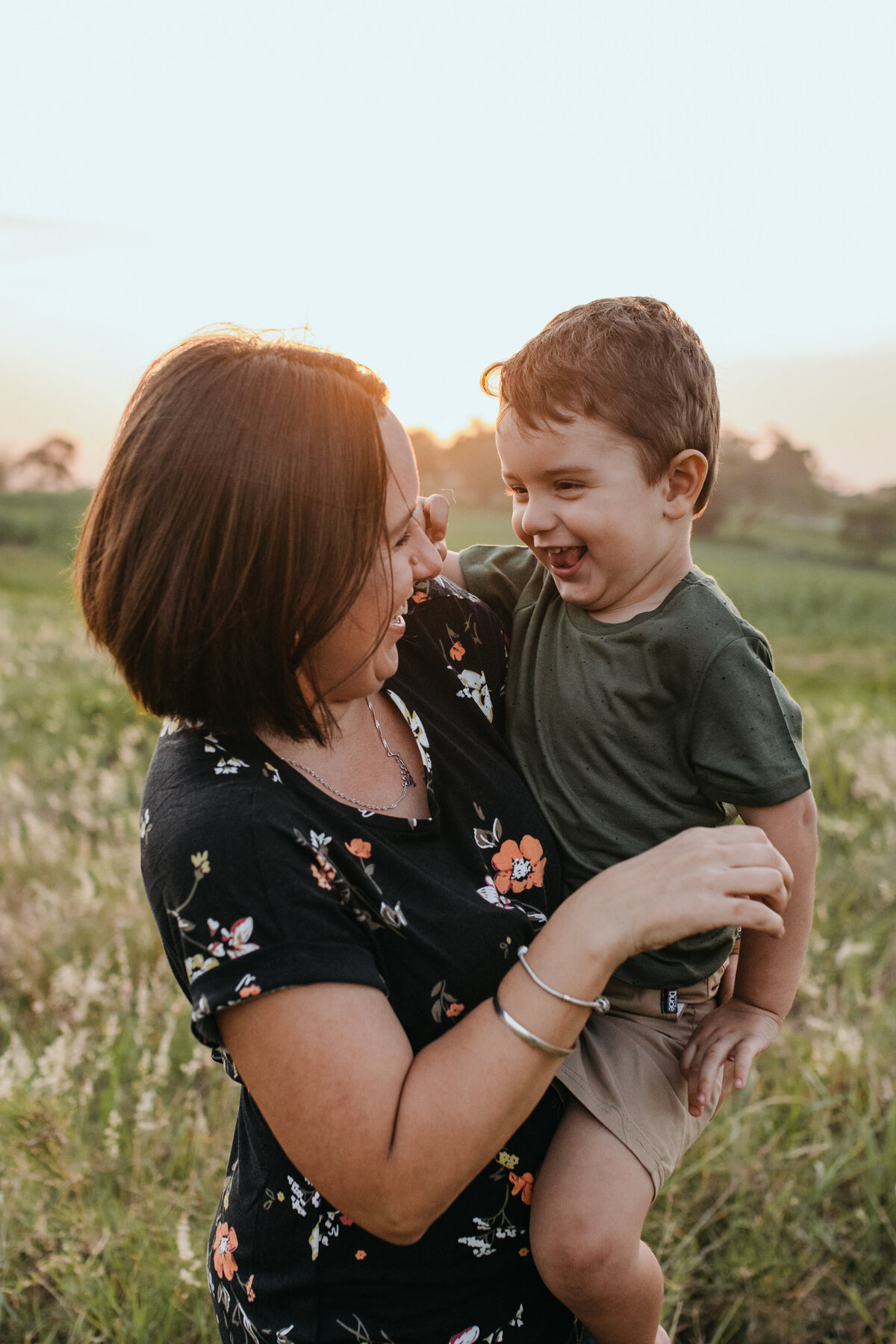 Bendigo family photographer capturing a joyful moment of a mother and her son playing and laughing together in a sunlit field.