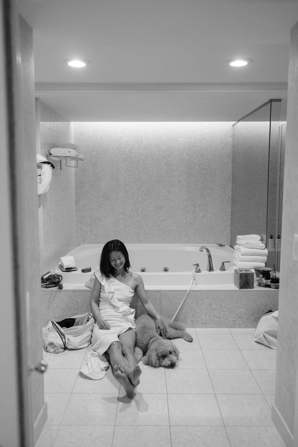 Bridesmaid sitting on the ground with her dog in the bathroom in black and white getting ready for Hawaii wedding at Four Seasons Oahu