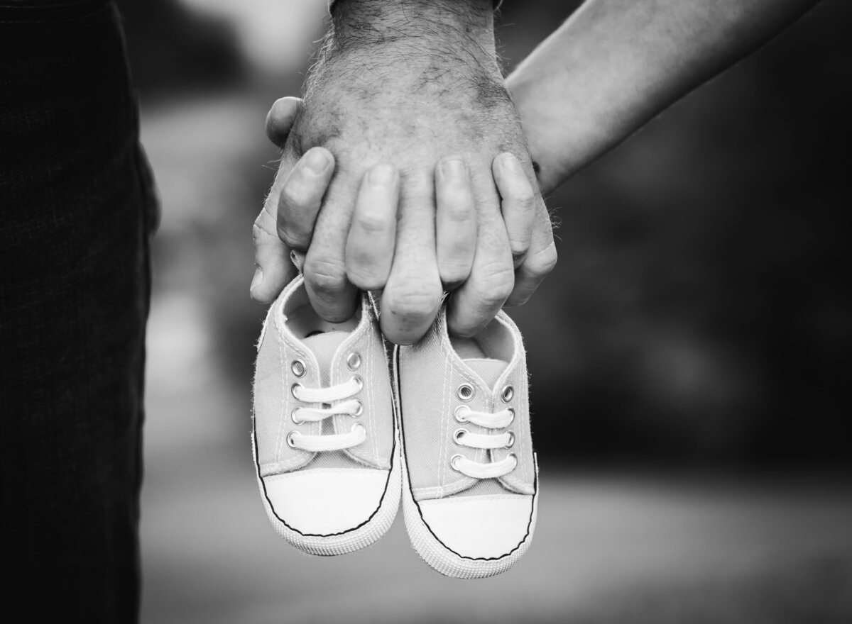 A couple holds baby shoes together, symbolizing their growing family