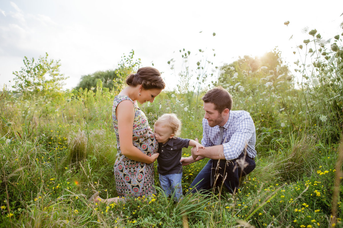 Expecting parents and toddler kissing belly in field - Jen Madigan - Naperville IL Maternity Photographer