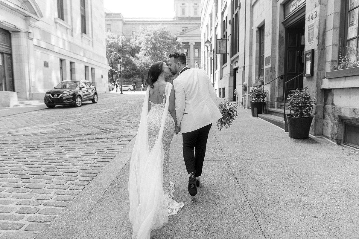 Les mariés, amoureux, s'embrassent en marchant dans une rue du Vieux Montréal.