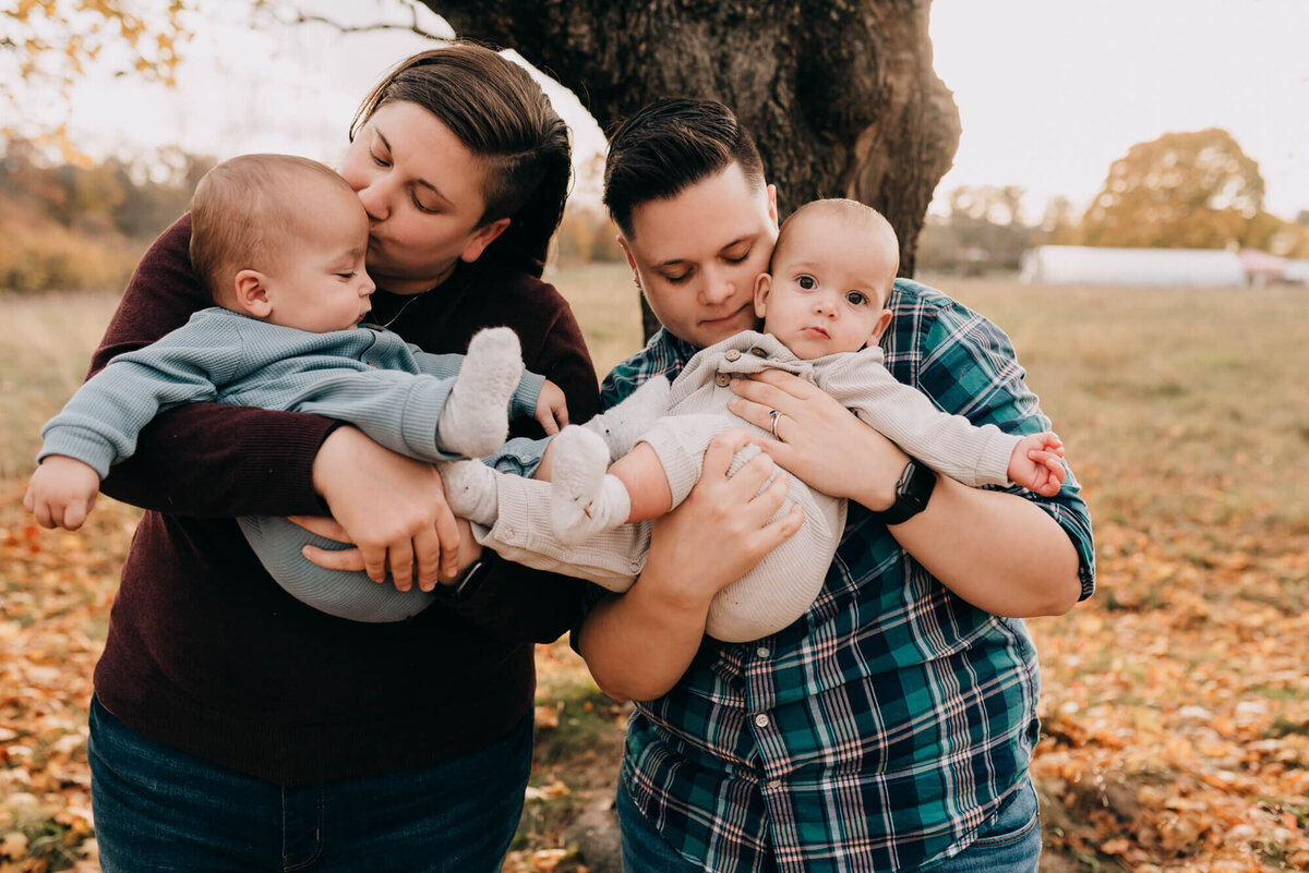 Two mothers hold their twin babies at sunset in a field during their photoshoot with Allison Wolf, Boston Family Photographer