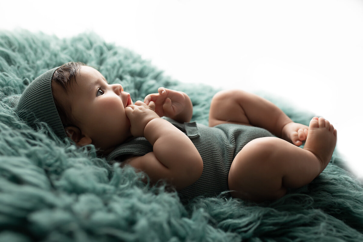 A baby in a green knit romper gazes toward the light while lying on a cozy textured blanket. This serene moment captured by a Dallas baby photographer highlights the gentle curiosity and tiny details that define milestone photography.