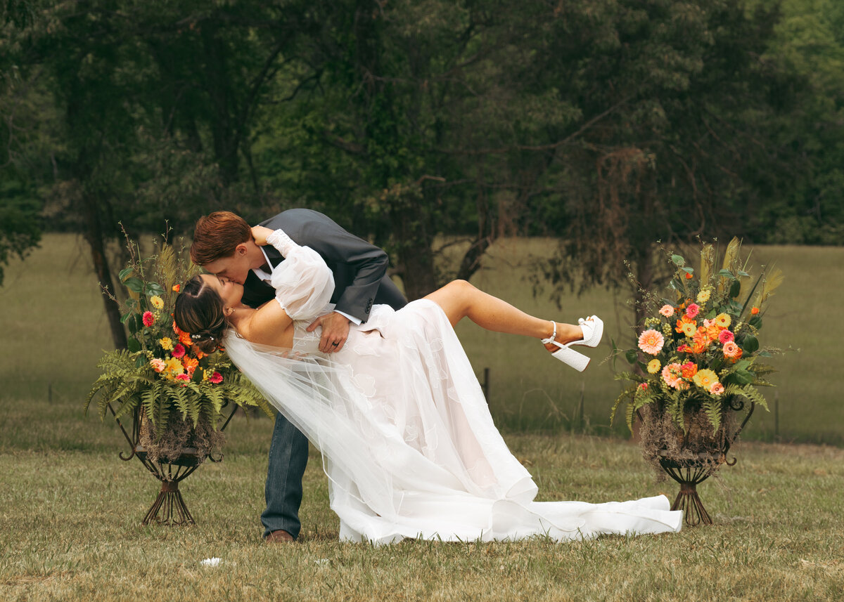 Colorful outdoor wedding in Tennessee — bride and groom dip kiss with floral aisle, captured by Nashville wedding photographer Kenzie Digitized.