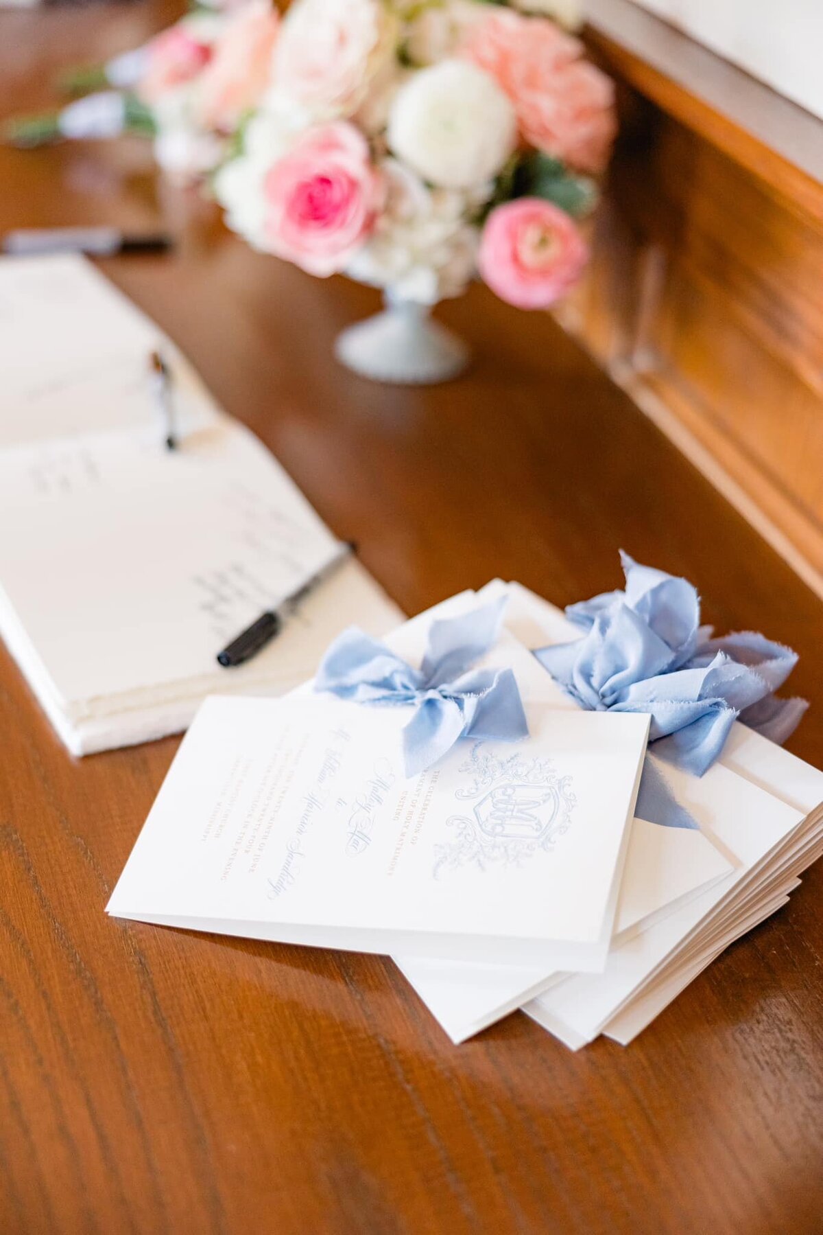 A stack of wedding programs with a dusty blue ribbon and the couple's wedding monogram.