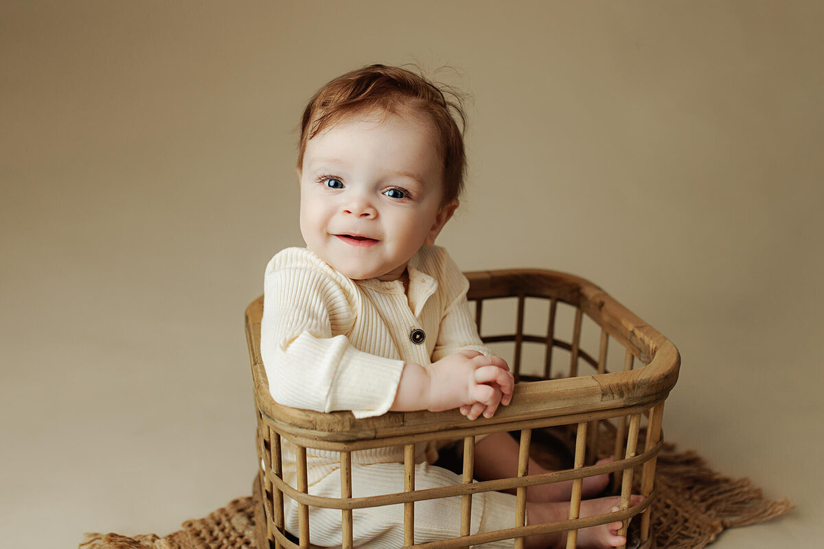 Eight month old little boy smiling in a bamboo crate.