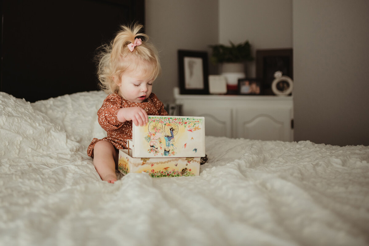 little girl sitting on the bed playing with jewelry box