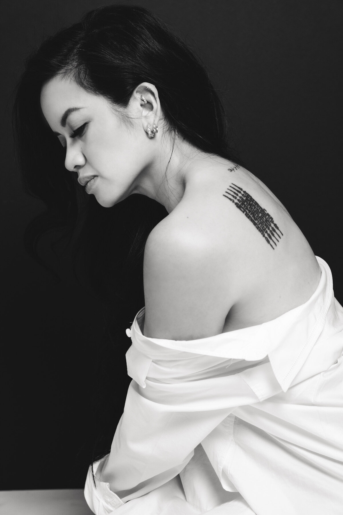 A black and white picture of a young Asian woman with a tattoo on her back.