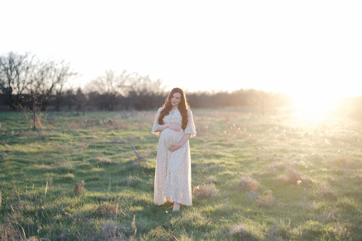 expecting mom in north fort worth embraces baby bump in a field at sunset