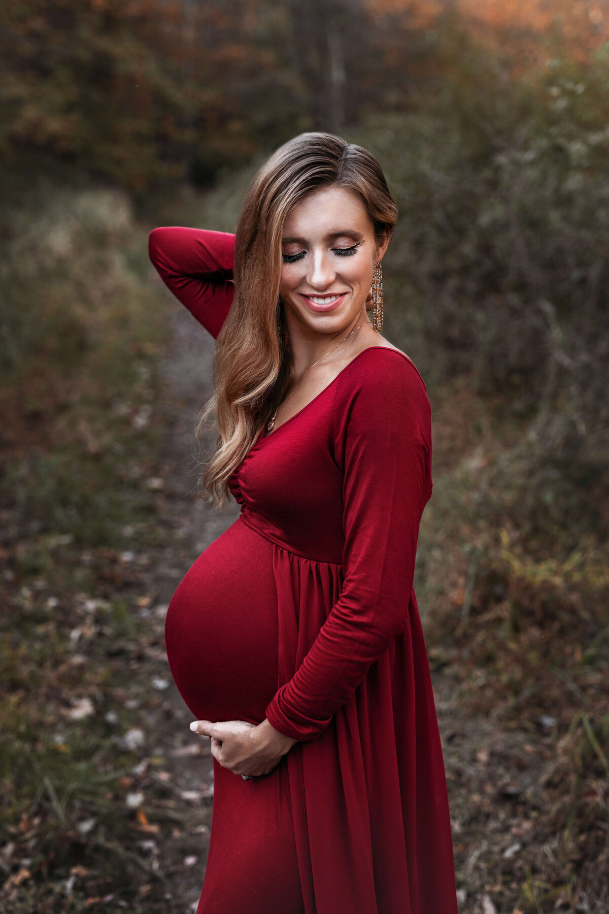 pregnant mother wearing a red maternity dress in the fall in the forrest at her maternity session