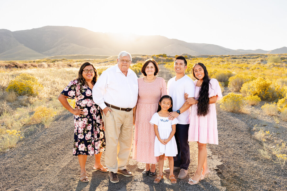 A multi-generational family standing together in a scenic desert landscape, dressed in pastel colors.