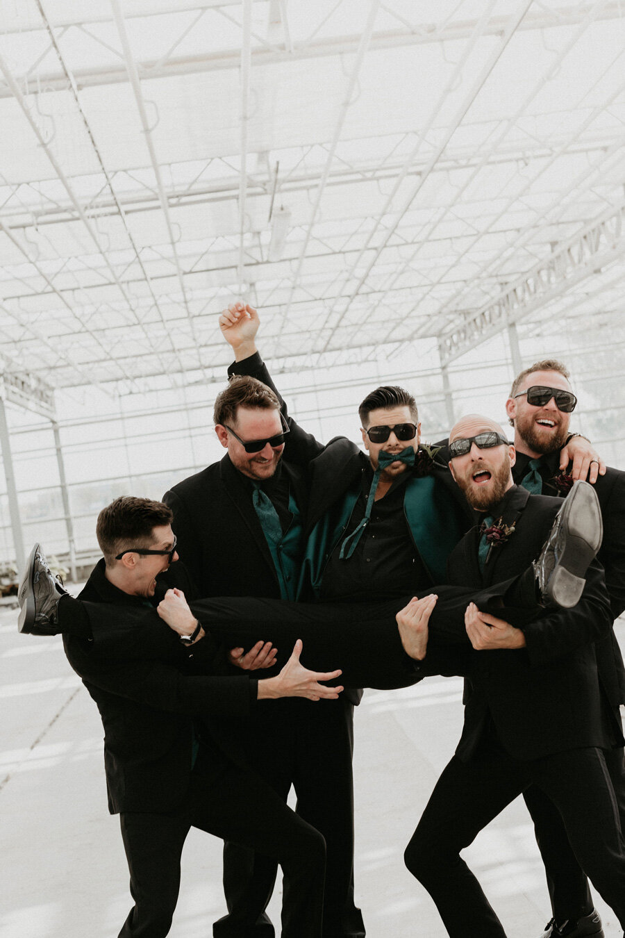 Groomsmen carrying groom with sunglasses on.
