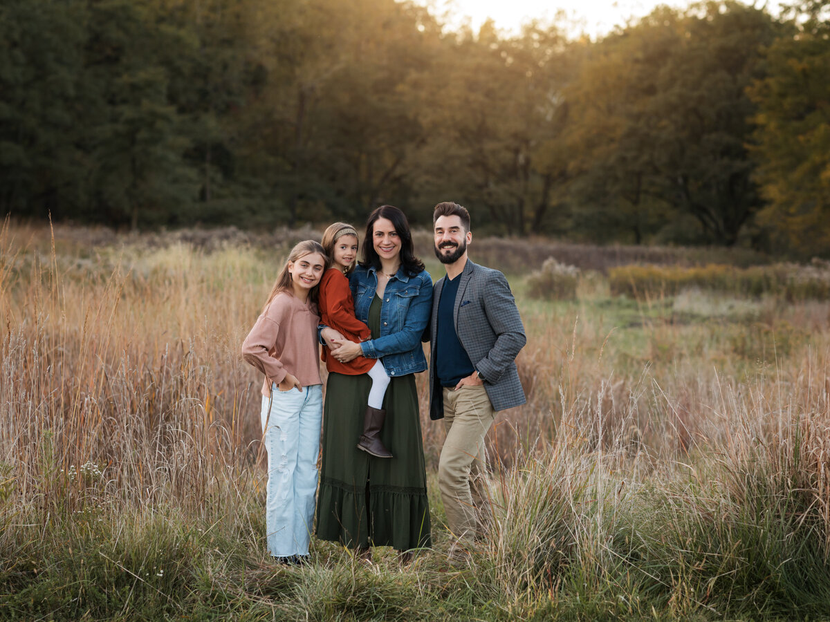 mom dad and two daughters posing in field for family photos cleveland family photography