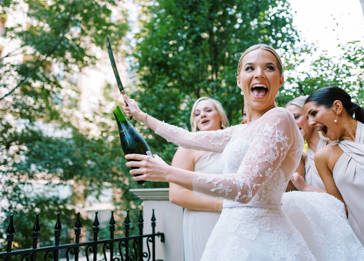 An excited shot of the bride after she opens a champagne bottle with a knife.  
