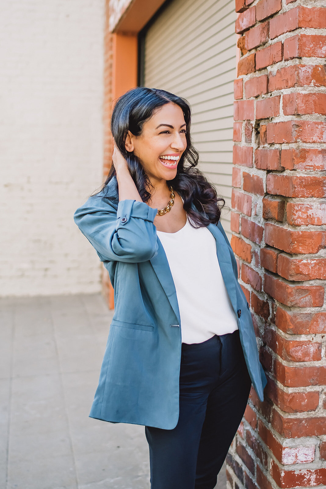 A woman in a blue blazer laughs and touches her hair for headshots.