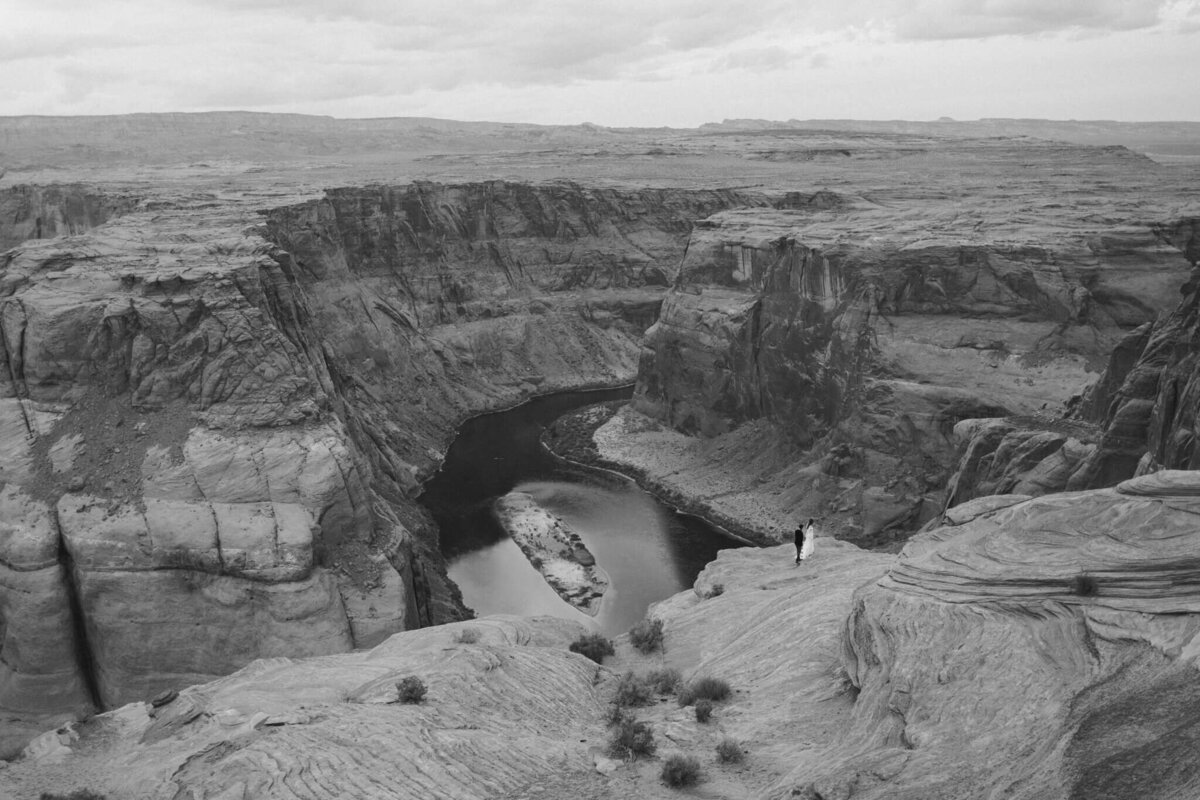 Een ultra wide shot bij horseshoe bend in Arizona, USA. In de verte zie je een bruidspaar lopen. Deze foto is in zwart wit en vastgelegd door Sharon Kastelijns Photography.