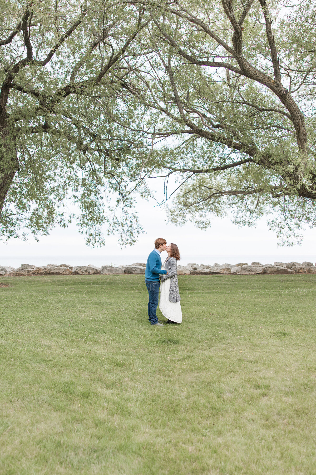 Expectant couple embracing each other and kissing under tall trees