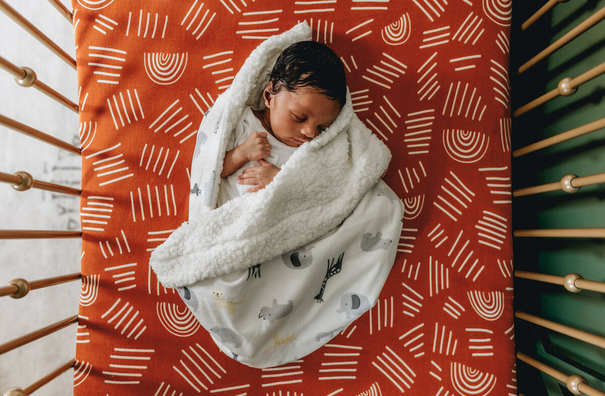 Infant photographer capturing a newborn baby sleeping in crib.