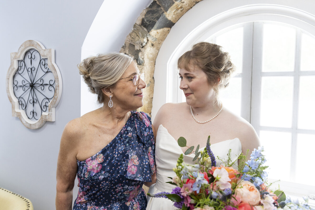 mother of the bride smiling at the bride holding her wedding bouquet
