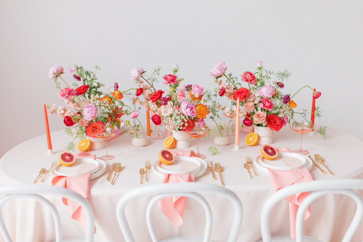 wedding table set with colorful florals, blood oranges, candles , white plates