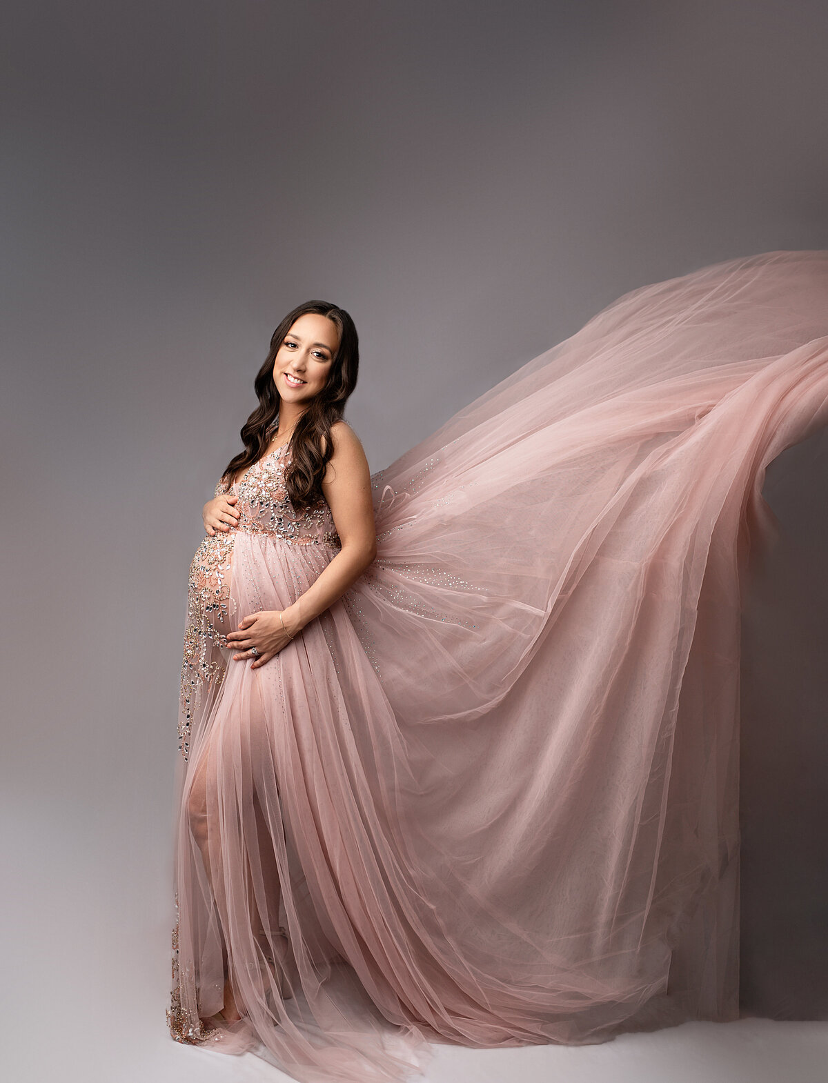 Mother in pink dress holds belly and smiles at camera