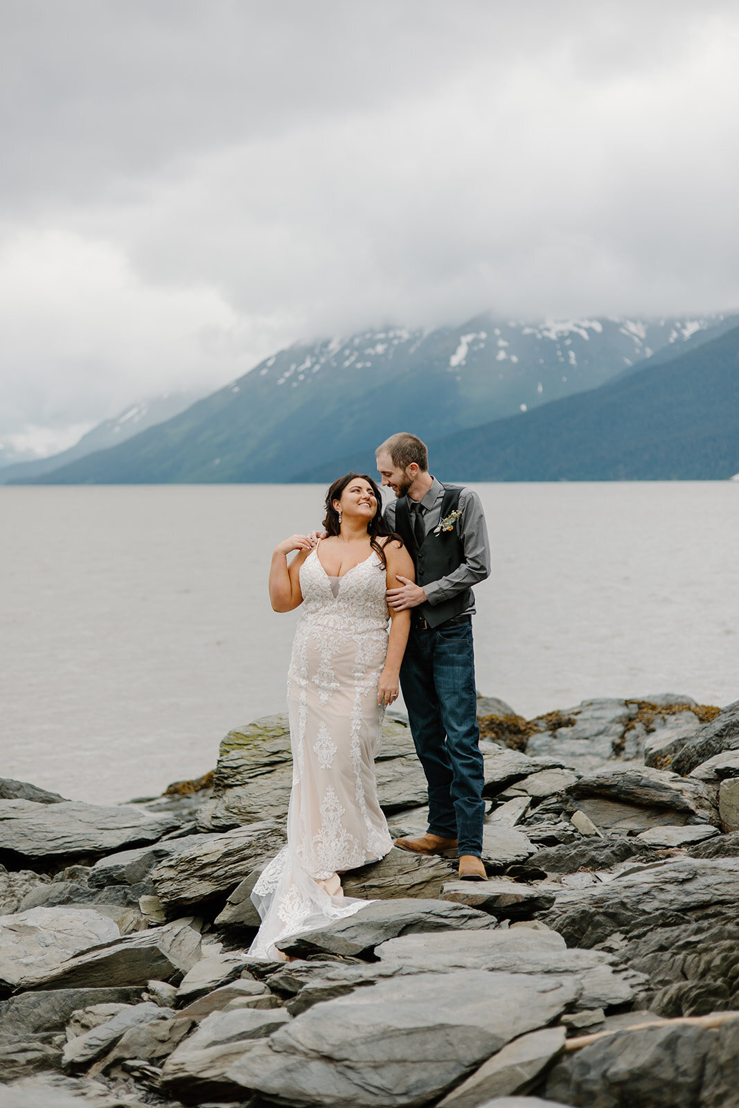 Elopement couple embraces on Alaska rock shoreline.