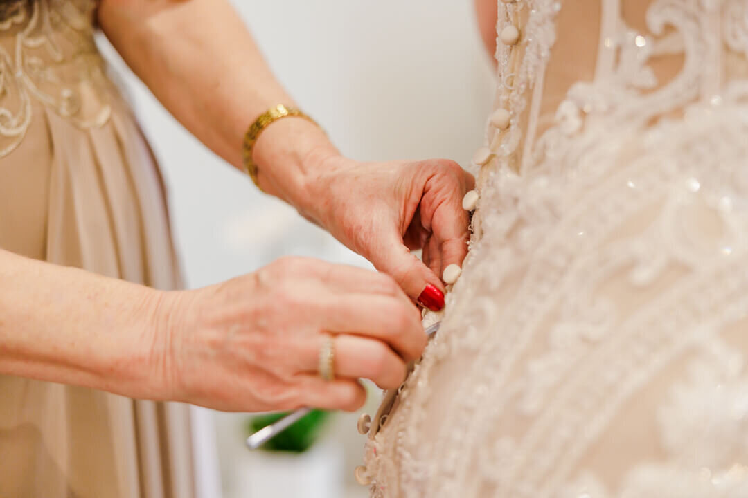 Details of mom buttoning in the bride into her dress
