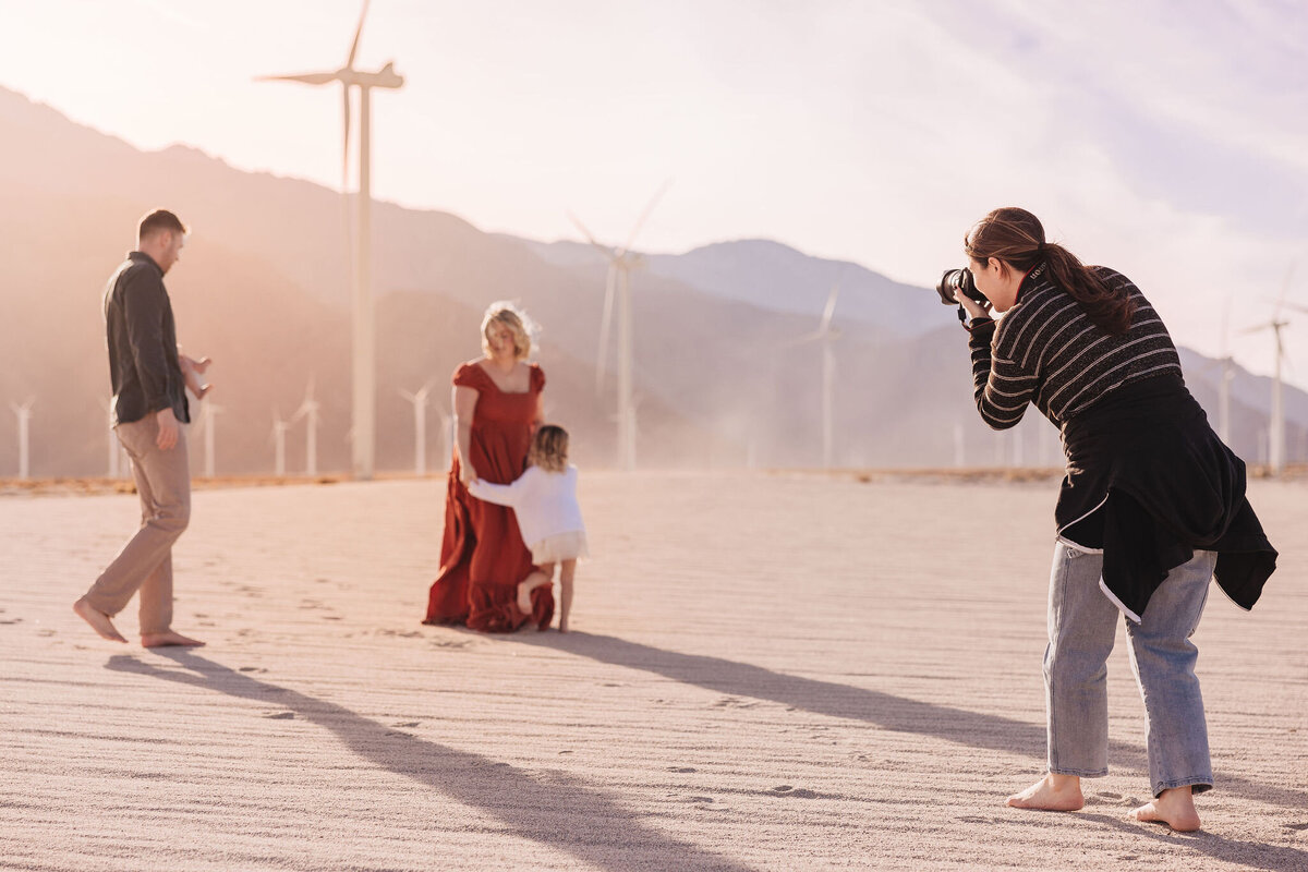 Photographer at family photoshoot on white sand and windmills in the background on a blogging for photographers page.