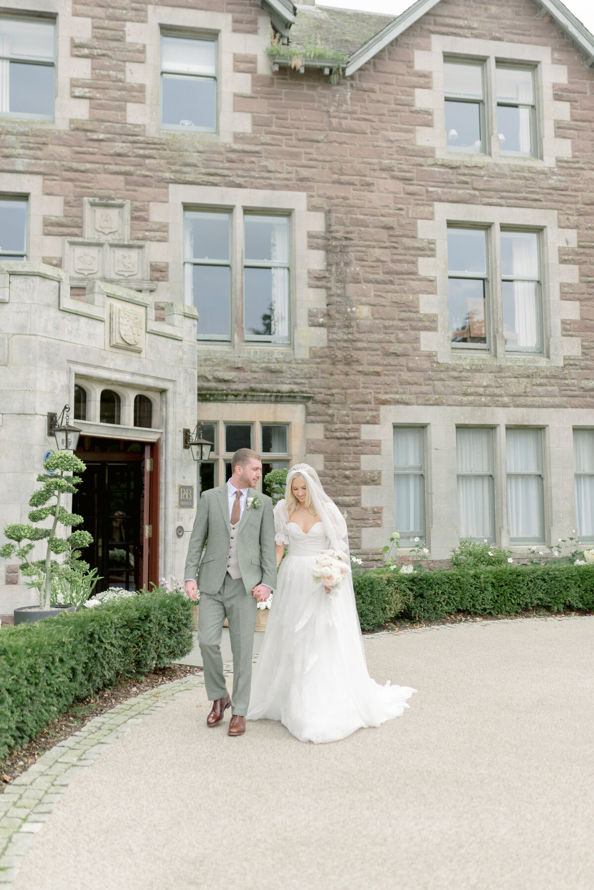 Bride, with cathedral length veil and silk wedding dress, and Groom, in tweed wedding suit, walking in the grounds of Cromlix House, photographed by Scotland fine art wedding photographer.