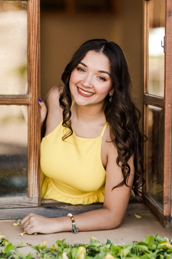 senior girl in yellow dress looking out window