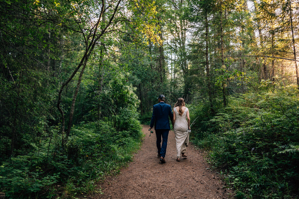 Bride and groom walk down pathway together that is lined with lush foliage.