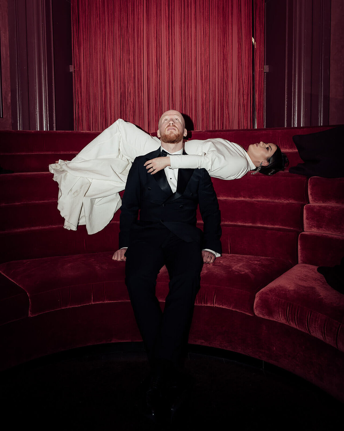 A bride is elevated behind and above her seated groom in the scarlet lounge in the Virgin Hotel Edinburgh.