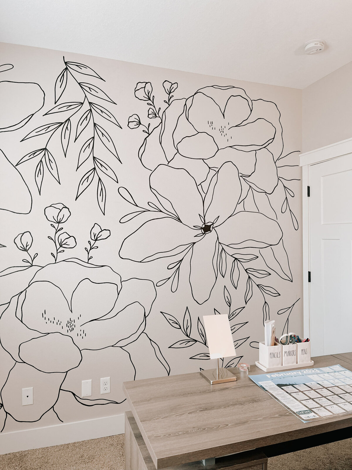 A home office featuring a desk and a white wall with modern black florals handpainted on it representing full service design and calligraphy by Life in Letters.