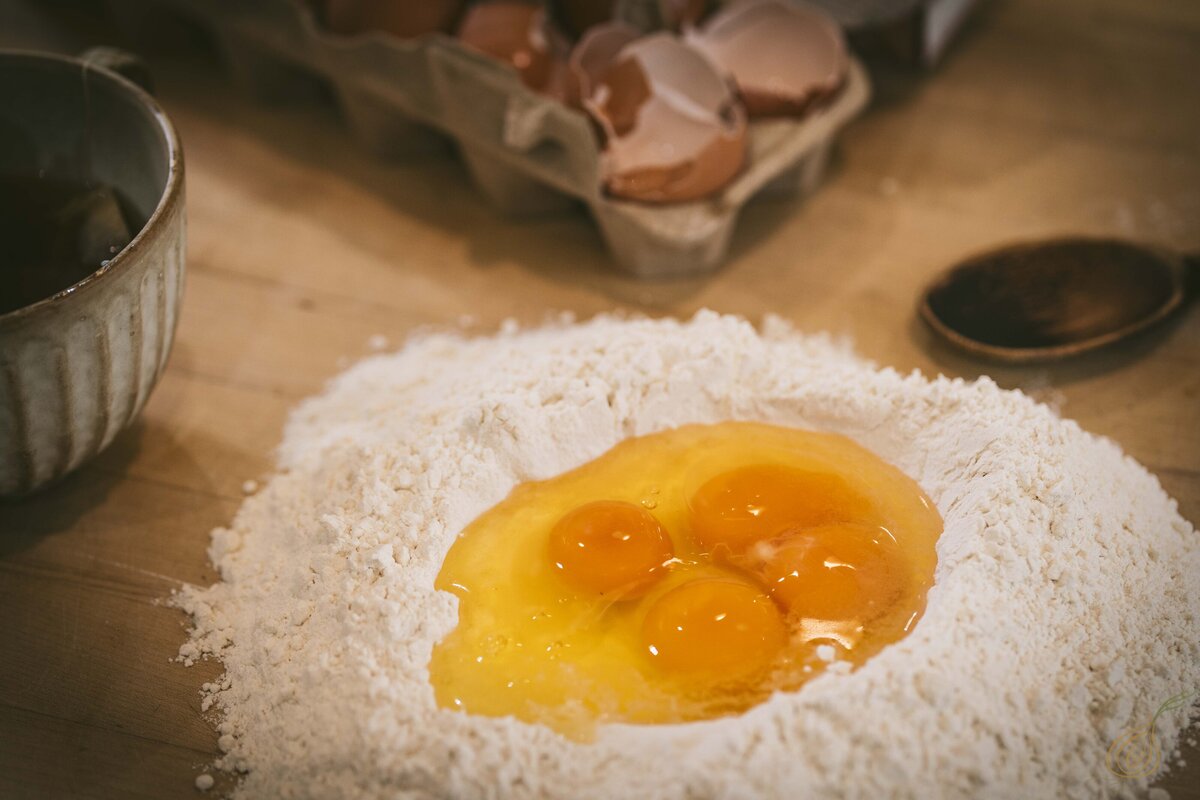 Fresh eggs placed in a pile of flour on a rustic table, illustrating the preparation for a culinary recipe.