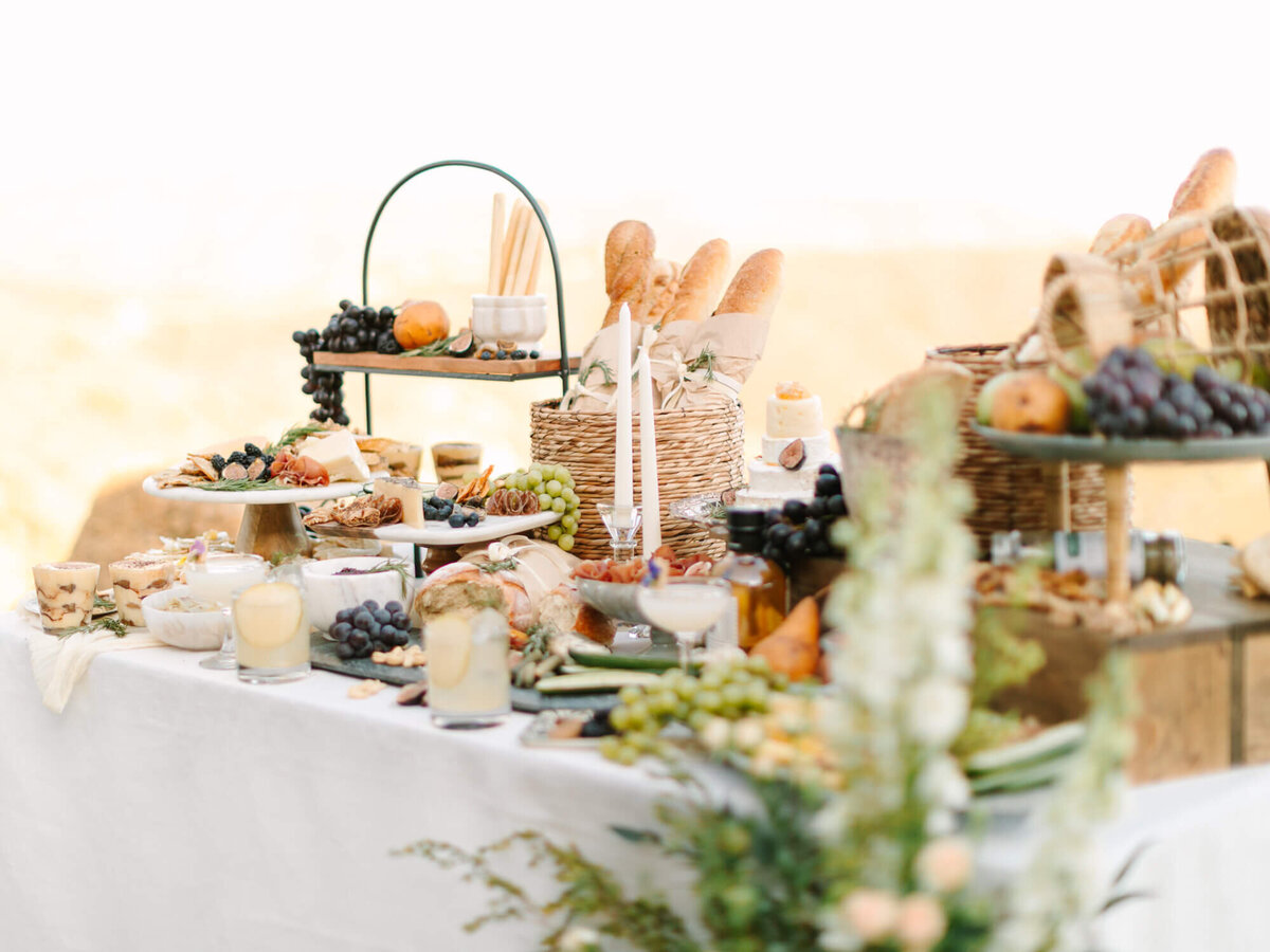 Elegant picnic spread with bread, cheeses, fruit, and candles on a white tablecloth.